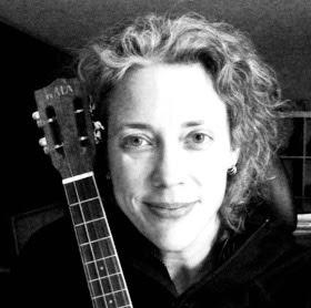 Black and white image of Lynn Tucker from the shoulders up and the neck of a guitar over one of her shoulders.